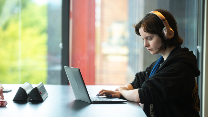 student with headphones on writing whilst sitting at a table